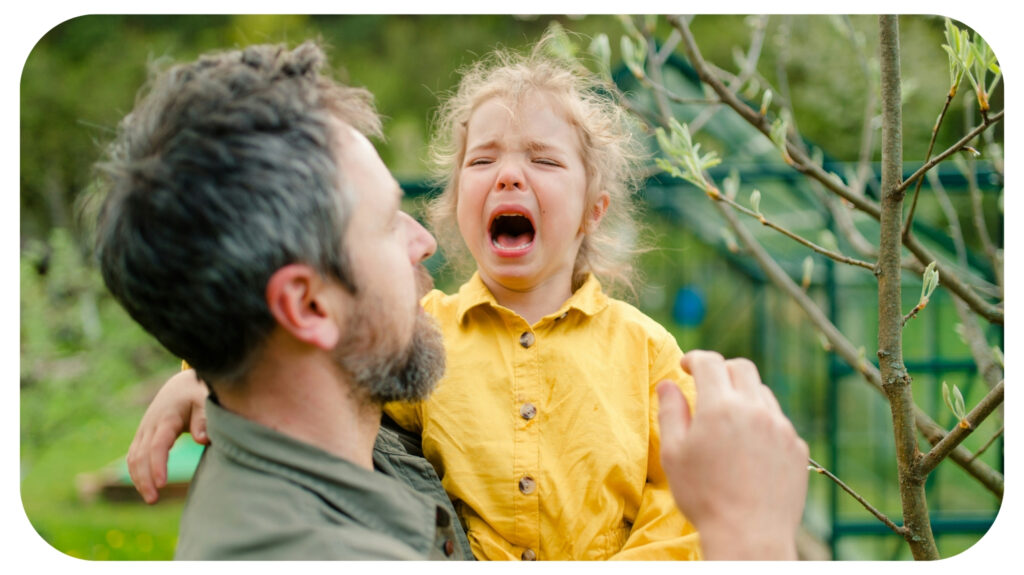 A father holding his crying little daughter and comforting her in garden.