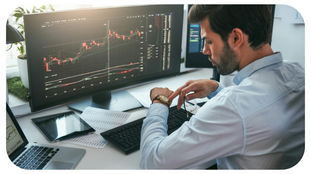 stock market broker looking at watch on his hand while working with data and charts on computer.