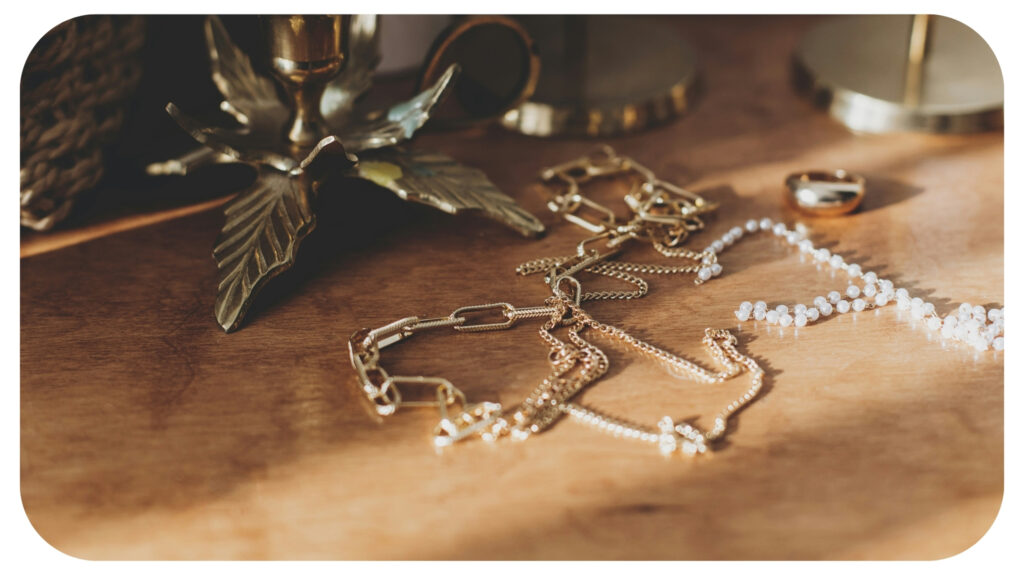 Stylish golden necklace and ring on wooden background in sunny light.