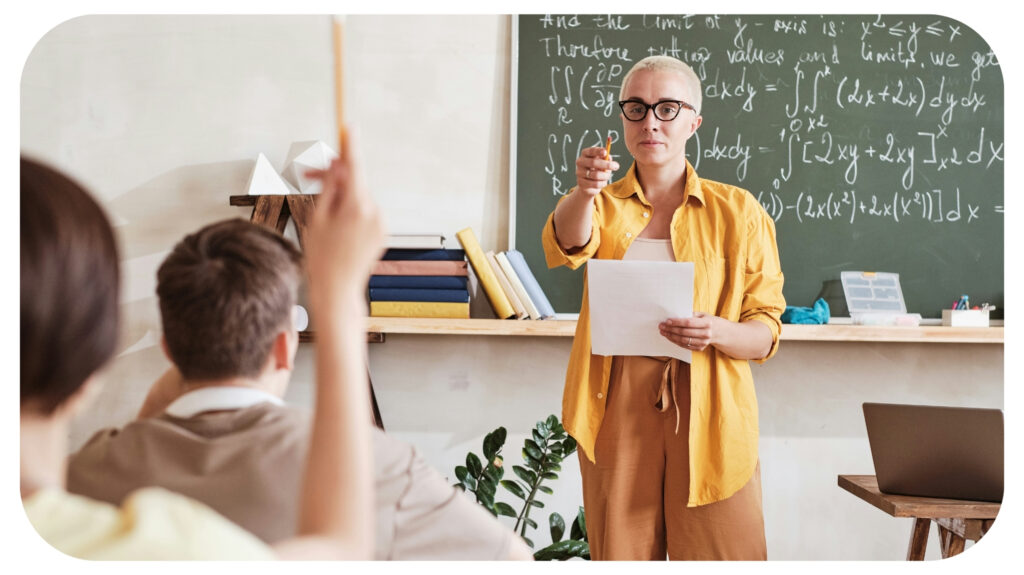 Teacher pointing at student who raising his arm and asking him a material during lesson at school.