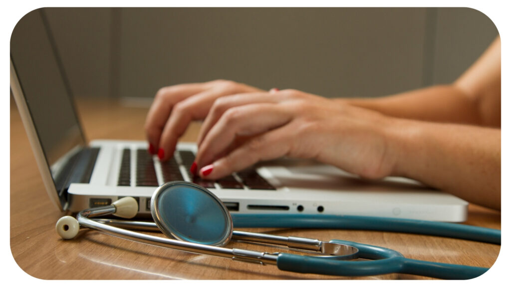 person sitting while using laptop computer and green stethoscope near.