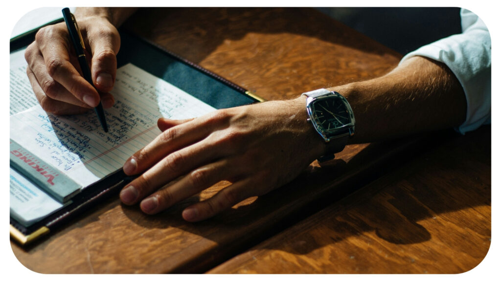 person writing on paper leaning on brown table.