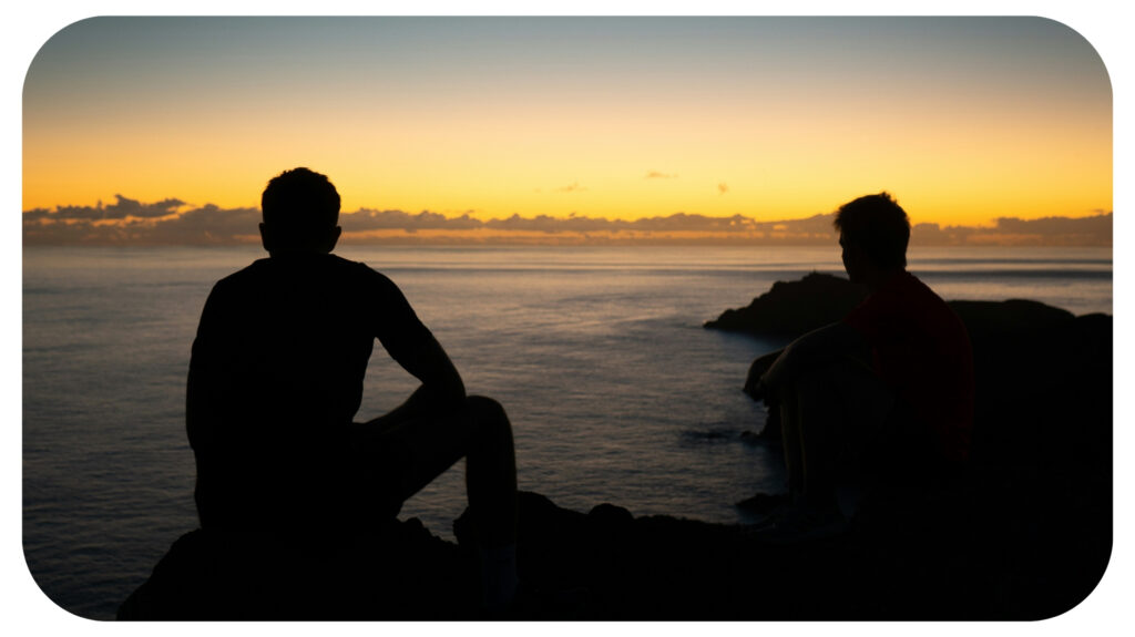 a couple of people sitting on top of a cliff.