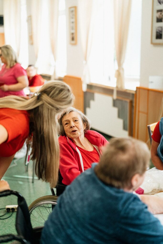Older woman engaged in conversation with a caregiver in a warm, social group setting.