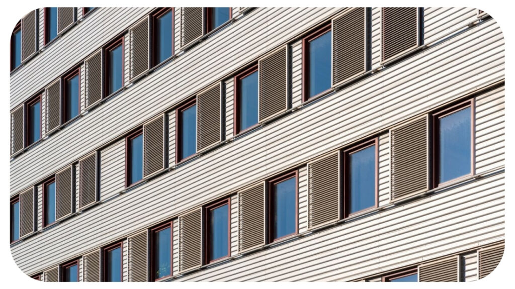 Angled view of a corrugated metal building facade with rows of windows and shutters.