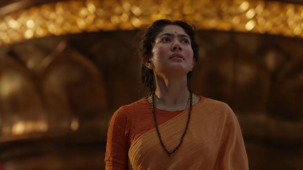 Sai Pallavi as Sita, wearing an orange sari and looking upward beneath an ornate golden arch in the Ramayana Part 1 trailer.
