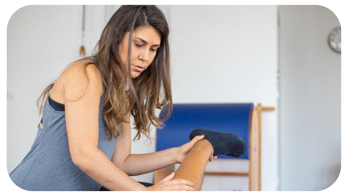 Physical therapist gently stretching a woman's leg during a rehabilitation session to improve mobility, flexibility, and support holistic injury recovery.