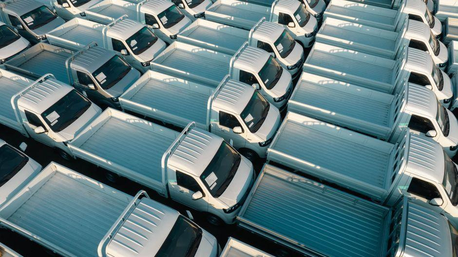 Aerial view of rows of white commercial trucks parked closely together in a vehicle storage lot.